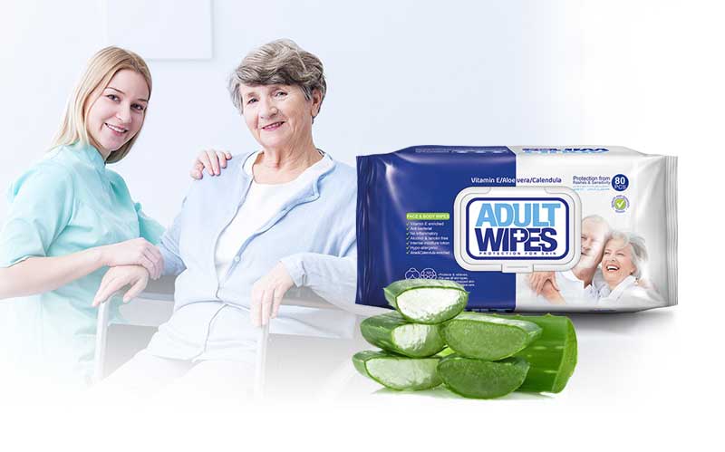 A caregiver assisting an elderly woman in a wheelchair, next to a large 80-pack of Sywipe aloe vera adult wipes, illustrating personal care wipes solutions for daily hygiene and senior skin care.
