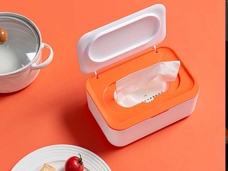 An orange and white baby wipe dispenser container open on a kitchen countertop, showcasing home storage solutions for baby wet wipes.