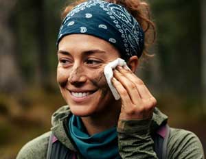 A smiling outdoor traveler cleaning her face with a refreshing wet wipe during a hike