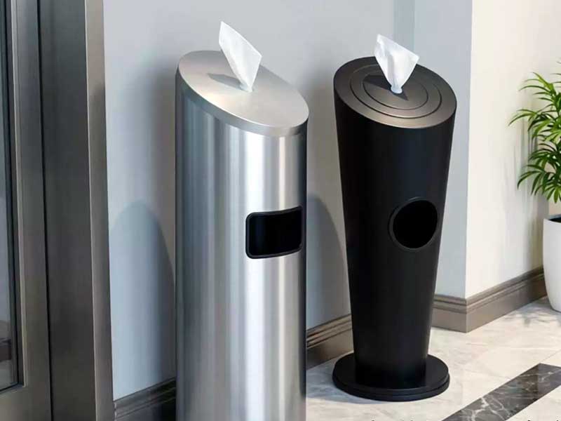 Stainless steel and matte black floor-standing gym wipes dispensers with integrated waste bins placed indoors for hygiene control.
