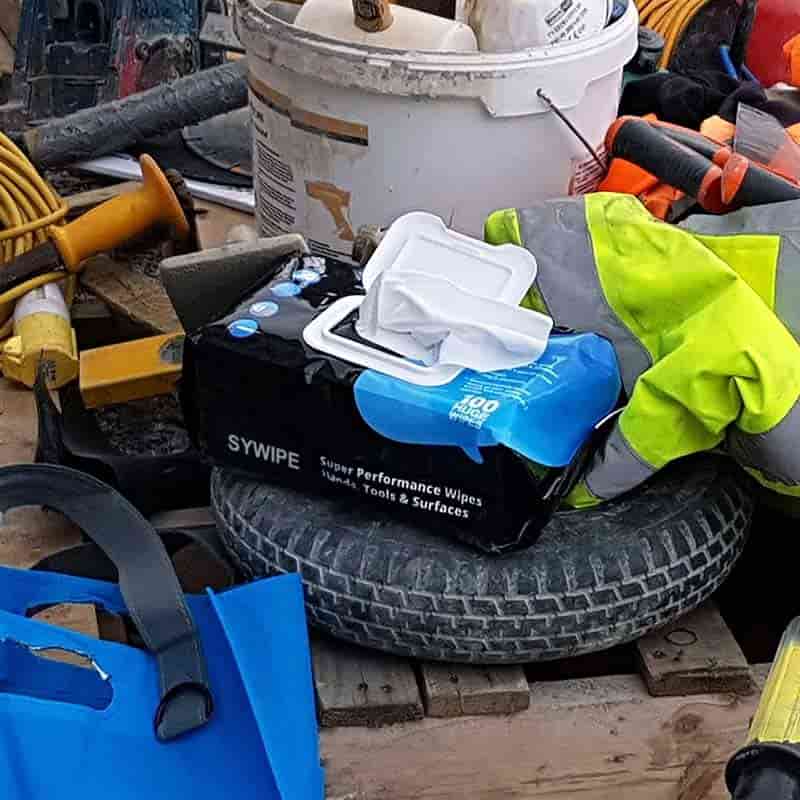 SYWIPE heavy duty industrial hand wipes placed on a tire at a messy construction site with tools and work gear