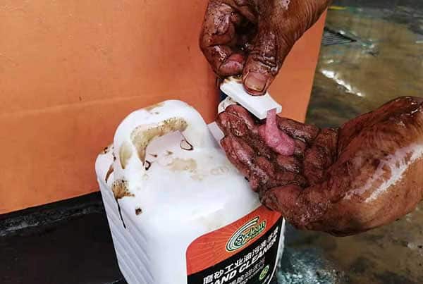 An industrial mechanic squeezing SYWIPE citrus-scented pumice hand cleaner onto grease-covered hands