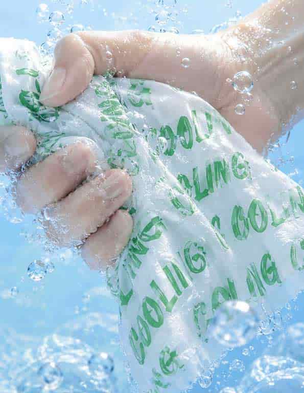 A hand squeezing an instant refreshing cooling wet wipe under splashing water, engineered to provide physical heat relief during sports or hot weather.