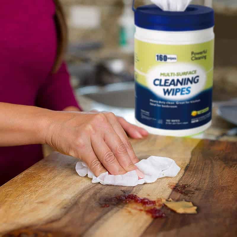 A multi-purpose cleaning wipe removing tough stains from a wooden surface next to a 160ct canister